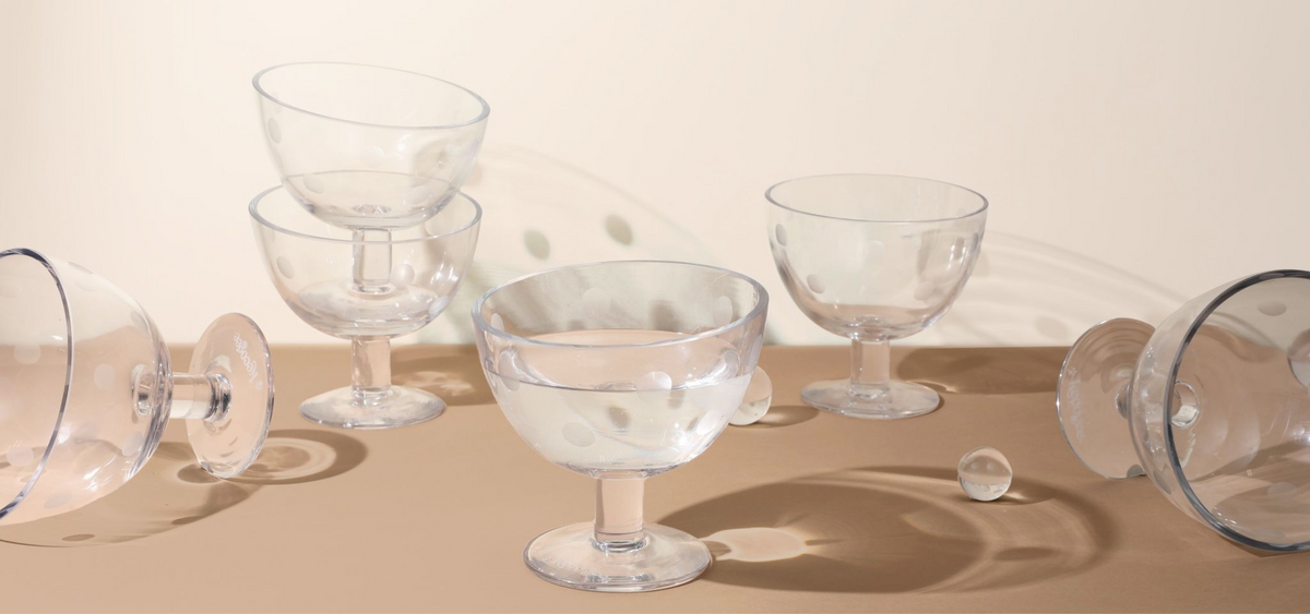 Clear glass dog bowls with dotted detail arranged upright and on their sides on a beige surface.
